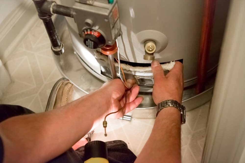 A man uses a flashlight to help him see the hot water heater in a dark closet